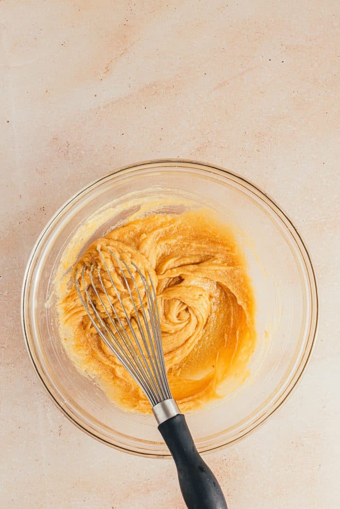 A glass bowl with cookie batter and a whisk.