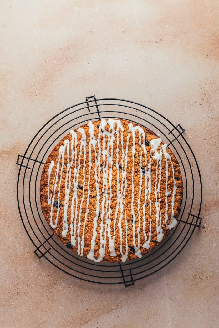 A blueberry sour cream coffee cake with drizzled icing on a cooling rack.