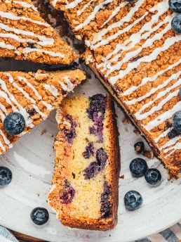 A blueberry coffee cake with slices cut out of it and one slice is turned on its side to show the blueberries.