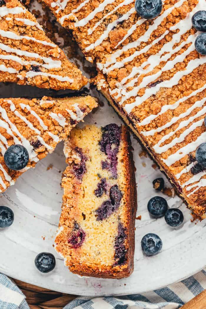 A blueberry coffee cake with slices cut out of it and one slice is turned on its side to show the blueberries. 