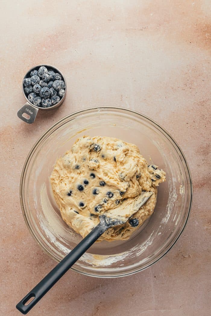 A glass bowl with cake batter mixed with blueberries.