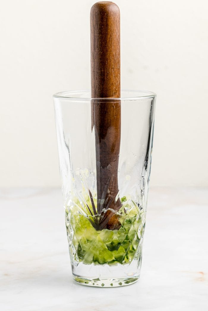 A glass with cucumbers being muddled. 