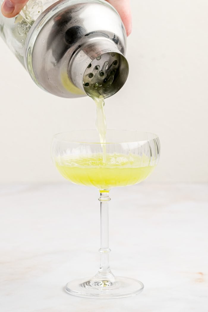 A cucumber Basil gimlet being poured into a cocktail glass.
