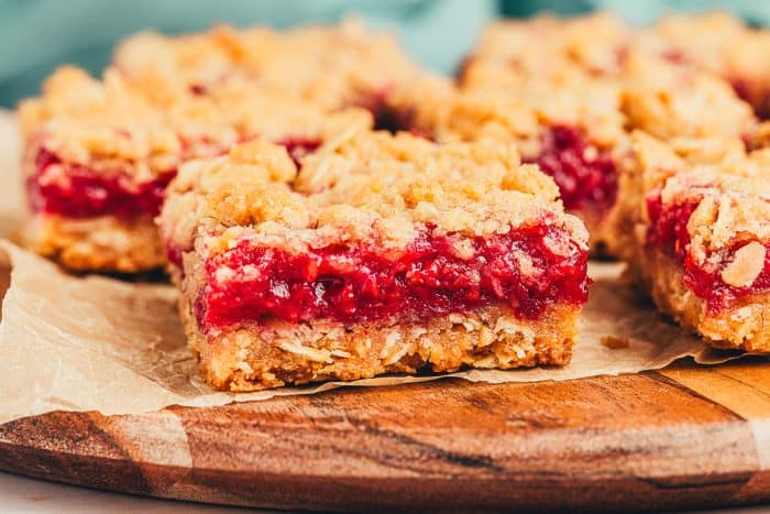 A couple of raspberry crumble bars on parchment paper on a wooden board.