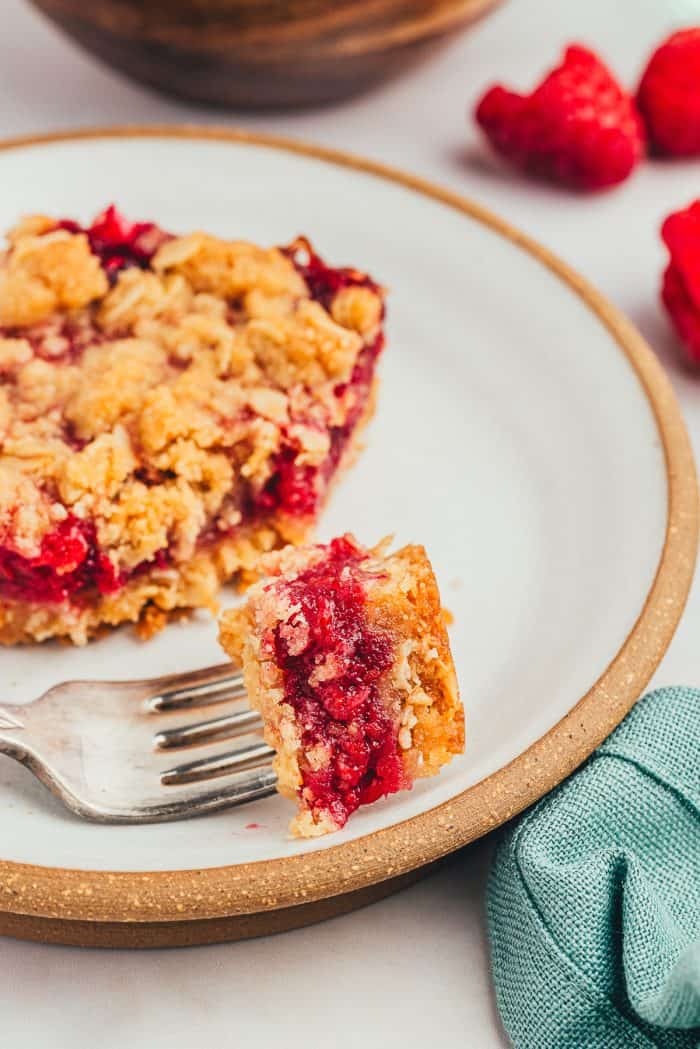 A white plate with a raspberry crumble bar with a fork taking a bite out of the bar.