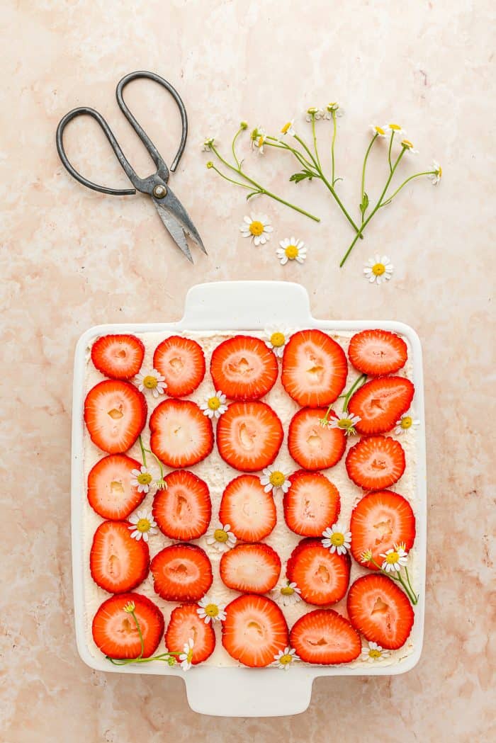 A white baking dish with strawberry tiramisu garnished with freshly sliced strawberries. 