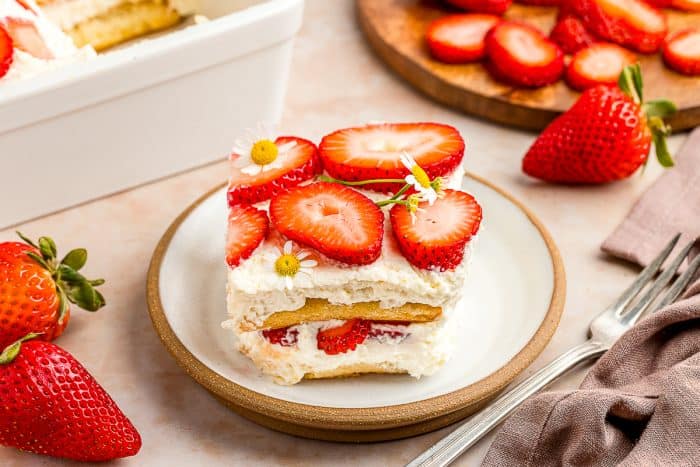 A slice of strawberry tiramisu on a white plate with a fork beside it.