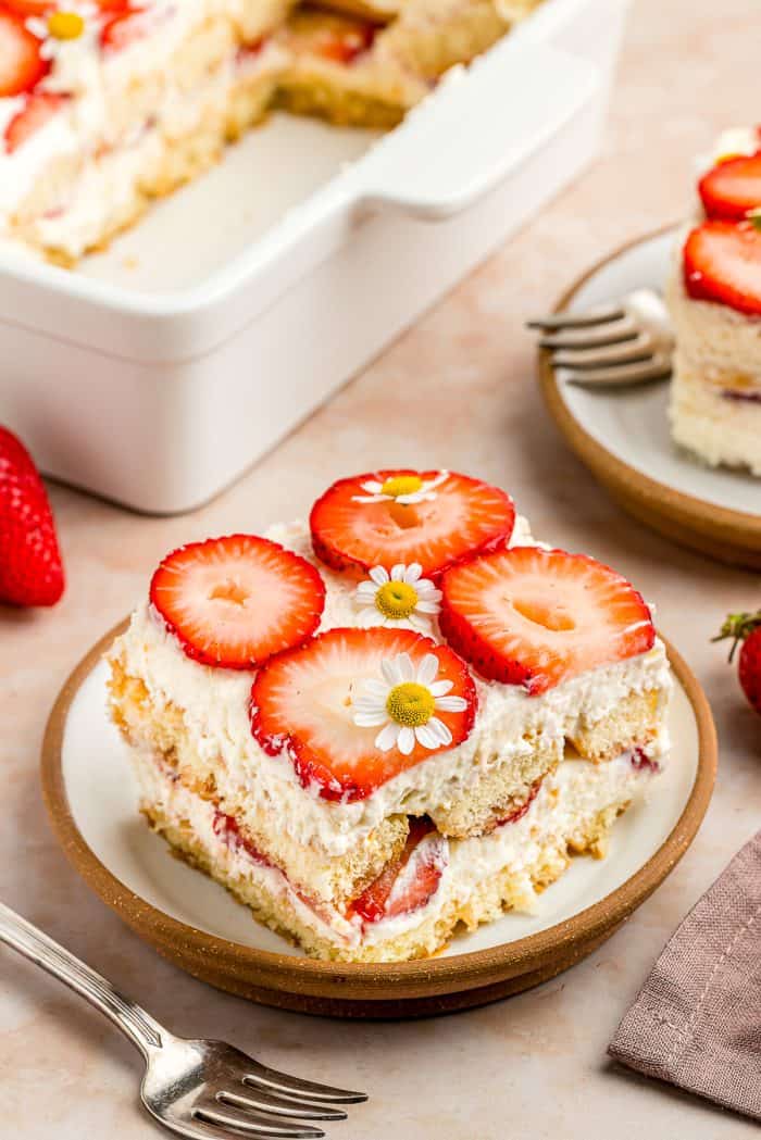 A slice of strawberry tiramisu on a white plate with a fork beside it.
