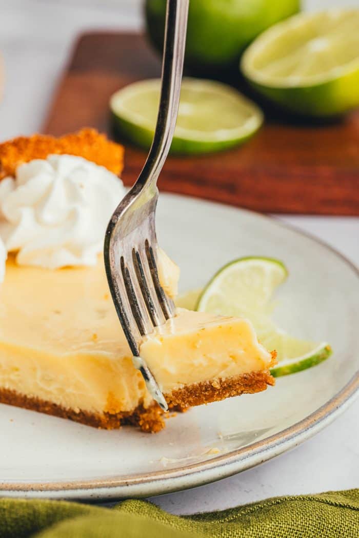 A slice of key lime pie on a plate with a fork being pierced into it. 
