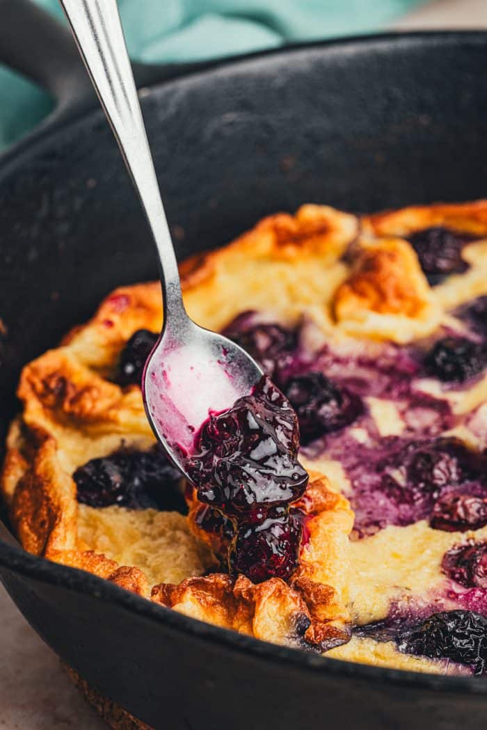 Adding homemade blueberry compote to a Dutch baby pancake.