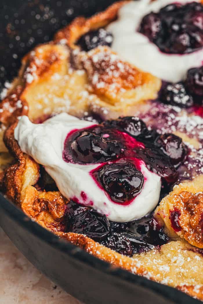 A closeup of a homemade blueberry Dutch baby pancake that is garnished with whipped cream and blueberries.