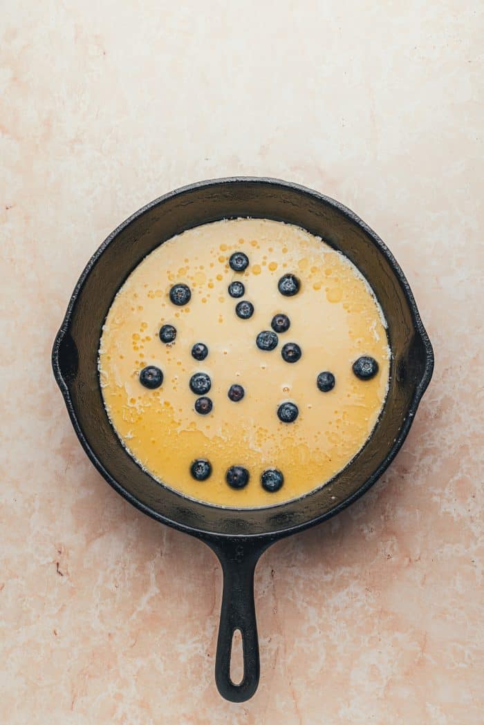 A hot skillet with Dutch baby pancake batter and blueberries.