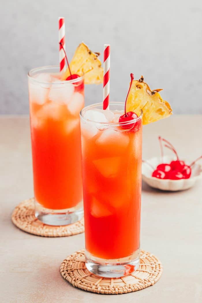 Two glasses filled with Planter's Punch and decorated with maraschino cherries and slices of pineapple.