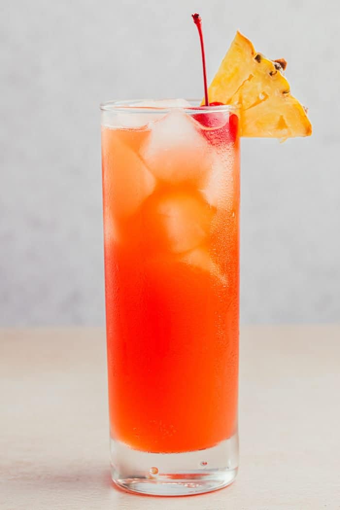 A glass filled with Planter's Punch and decorated with a maraschino cherry and a slice of pineapple.