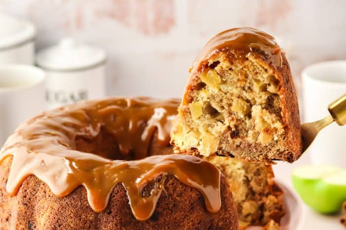 An image of a slice of caramel apple Bundt cake on a cake lifter being removed from the whole cake.