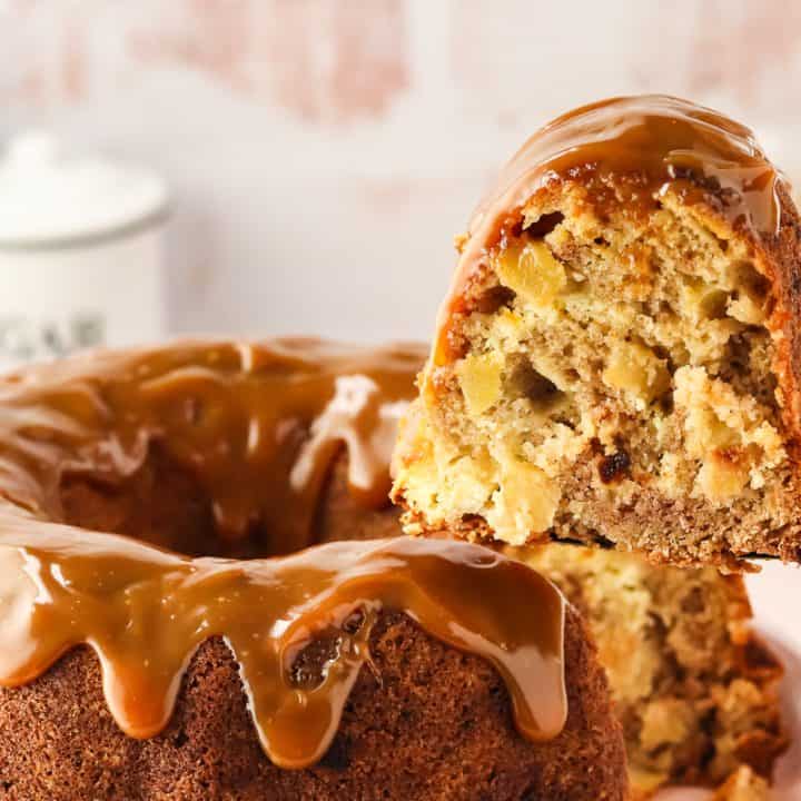 An image of a slice of caramel apple Bundt cake on a cake lifter being removed from the whole cake.