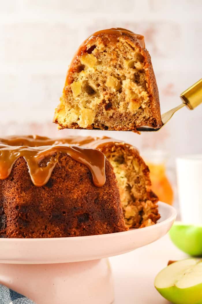 An image of a slice of caramel apple Bundt cake on a cake lifter being removed from the whole cake.