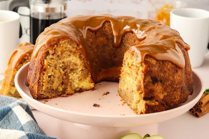 A caramel apple Bundt cake with slices removed from it on a white cake plate.