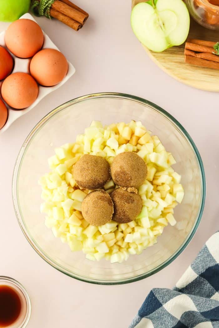 Brown sugar over diced apples in a glass mixing bowl.