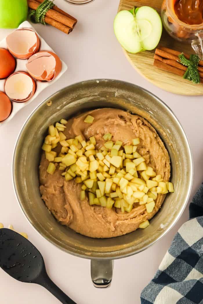 Diced apples over cake batter in a metal bowl.