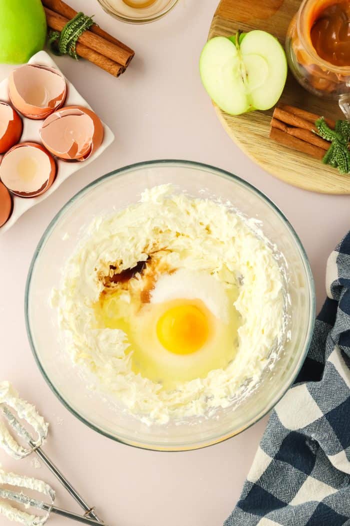 An egg with cream cheese and vanilla in a glass mixing bowl.