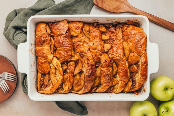 A white dish with baked croissant french toast with apples.