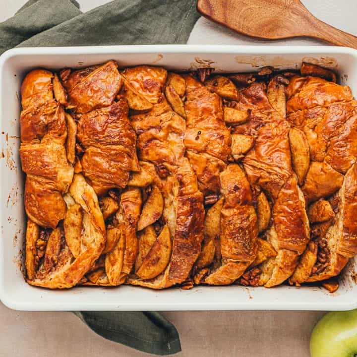 A white dish with baked croissant french toast with apples.