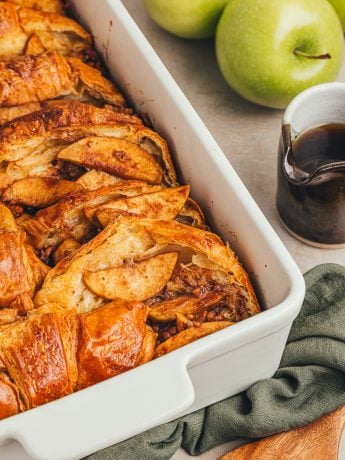 A white dish with baked croissant french toast with apples.