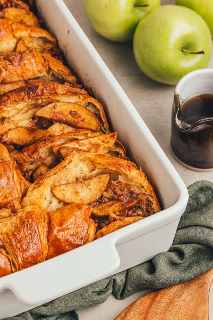 A white dish with baked croissant french toast with apples.