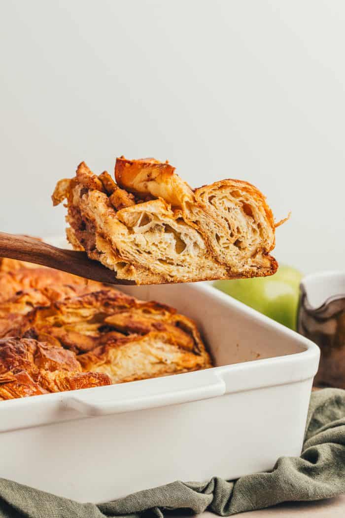 A slice of apple french toast bake being removed from a white baking dish.