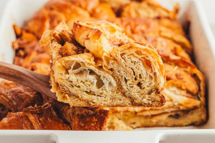 A slice of apple french toast bake being removed from a white baking dish.