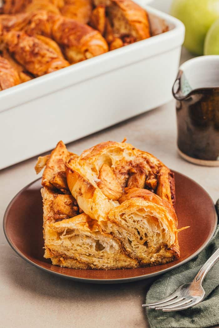 A slice of apple french toast bake on a maroon colored plate.