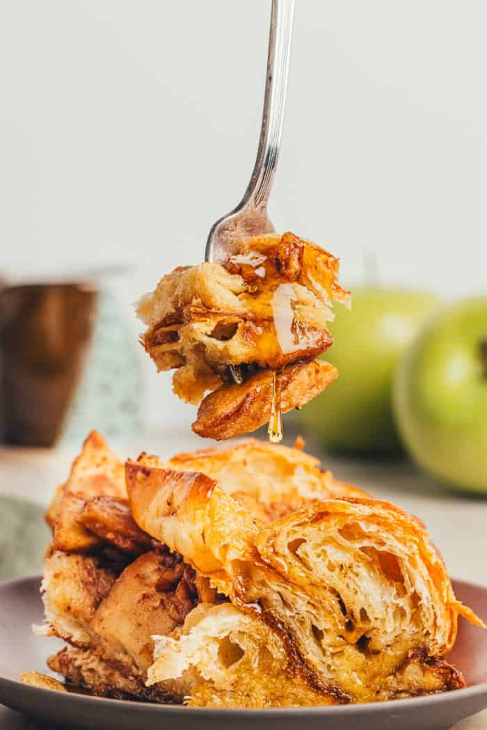 A slice of apple french toast bake on a brown colored plate with a fork taking a bite out of it.