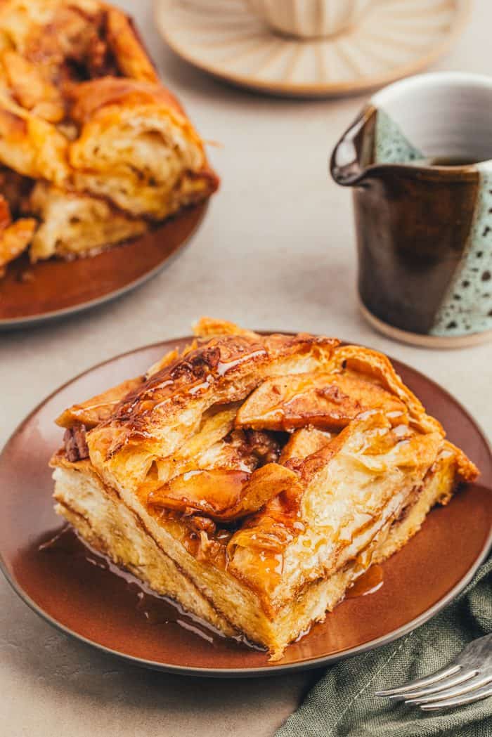 A slice of apple french toast bake on a brown colored plate.