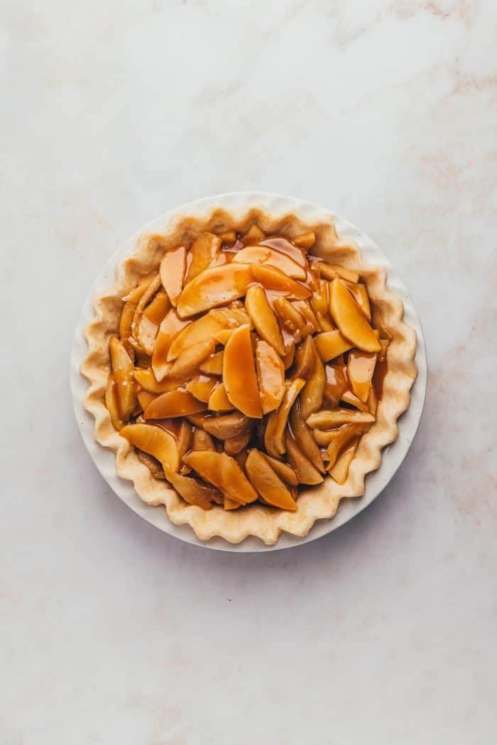 An unbaked pie with the raw apple pie filling and caramel sauce over it. 