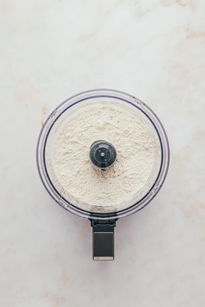 A food processor with flour, sugar, and salt.