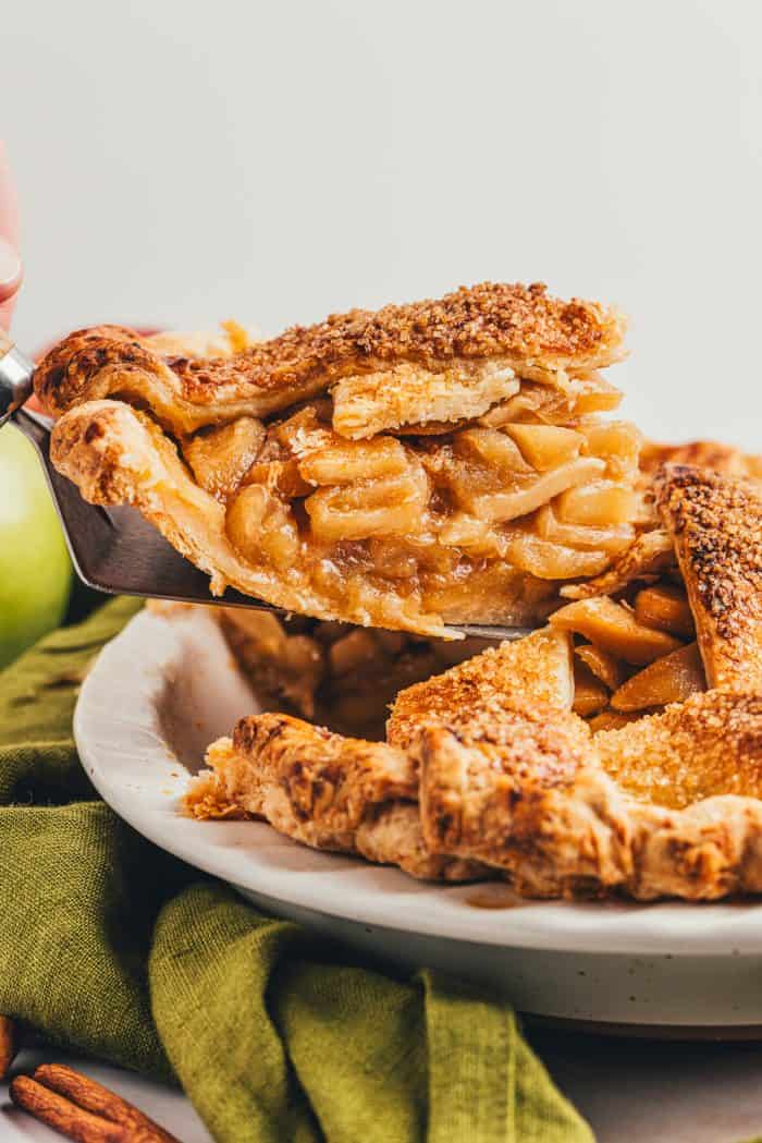 A slice of apple pie being removed from a whole pie with a green napkin.