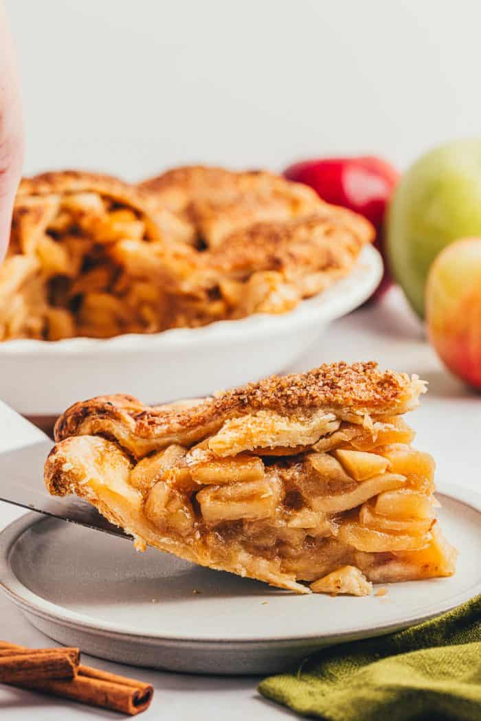 A slice of apple pie being placed on a white plate.