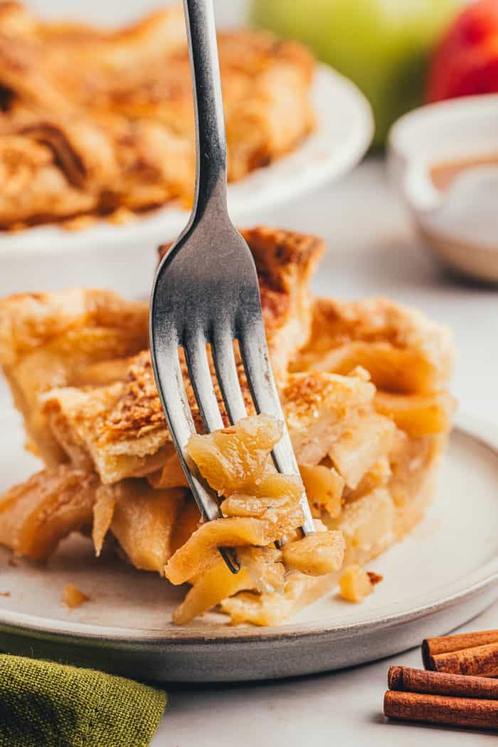 A slice of apple pie with a fork taking a bite out of it.