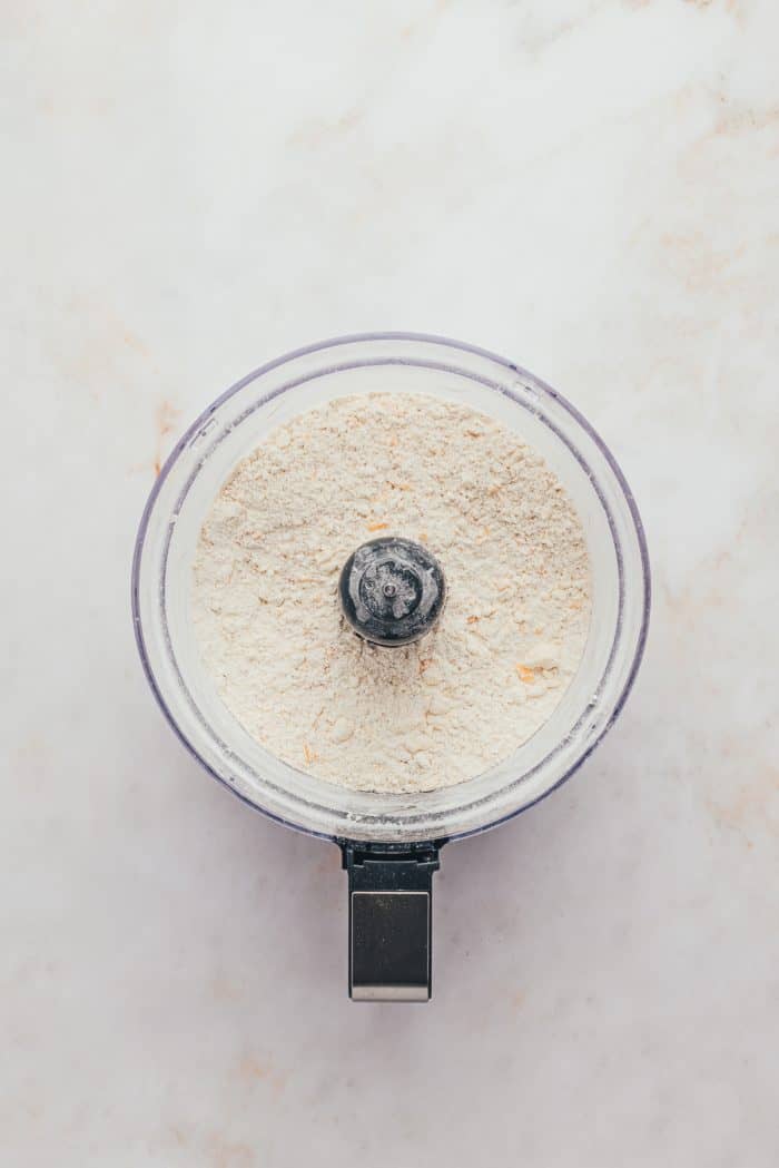 A food processor with flour, sugar, salt. and some butter.