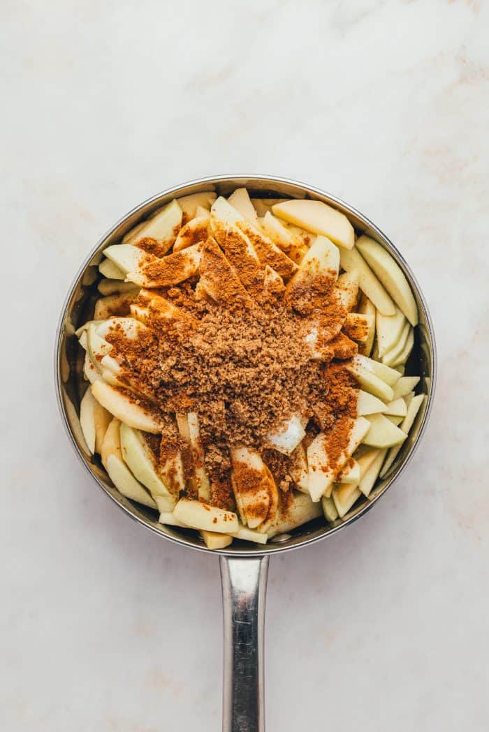 A skillet with sliced apples and cinnamon and sugar sprinkled over them.