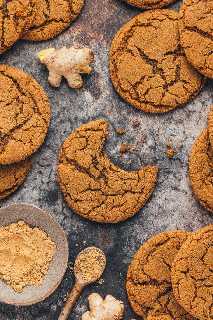 A couple of chewy molasses cookies on a dark surface and one has a bite taken out of it.