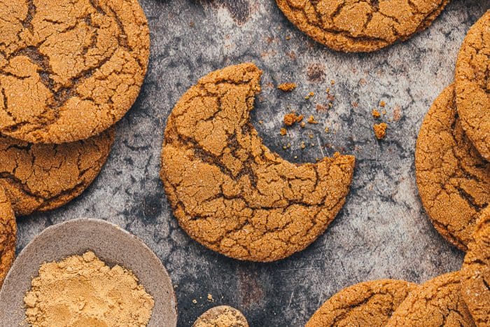 A couple of chewy molasses cookies on a dark surface and one has a bite taken out of it.