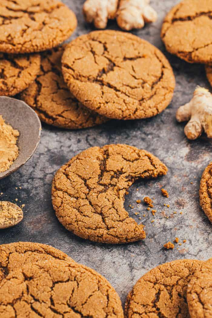 A couple of chewy molasses cookies on a dark surface and one has a bite taken out of it.