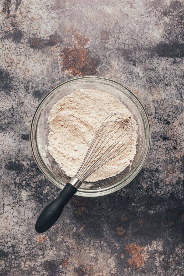 A glass bowl with flour and baking agents added to it with a whisk.