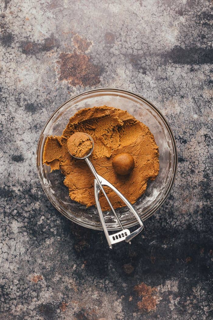 A bowl of ginger molasses cookie dough that is being scooped into balls.