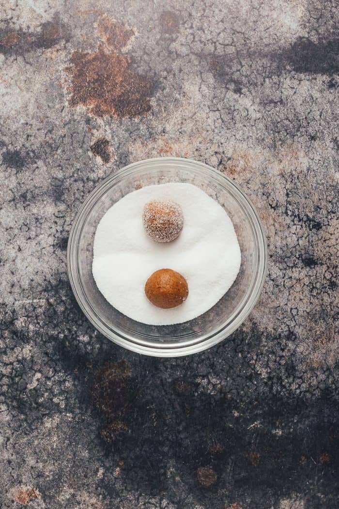 A bowl of sugar with ginger molasses cookie dough balls.