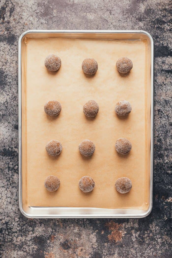 A cookie tray with unbaked ginger molasses cookies that are in ball shapes.