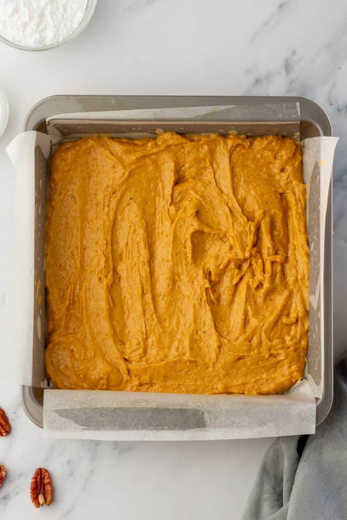 The pumpkin cake batter in a cake pan with parchment paper.