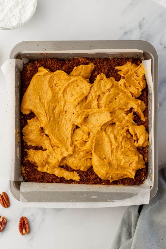 The pumpkin cake batter with a layer of cinnamon sugar, and dabs of pumpkin cake batter in a cake pan with parchment paper.